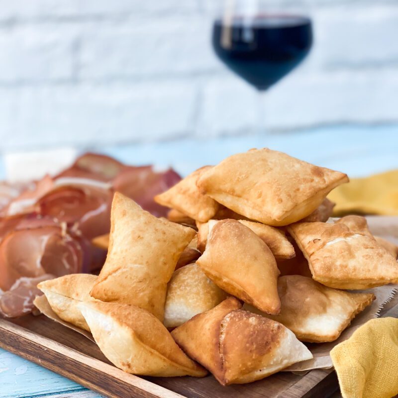 gnocco fritto on a wooden board with a glass of red wine in the background