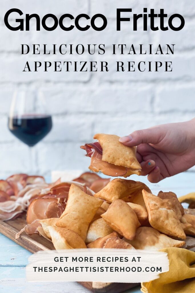 a hand holding a gnocco fritto with prosciutto in it, on the backgtround a glass of red wine and under a board of meat and cheese