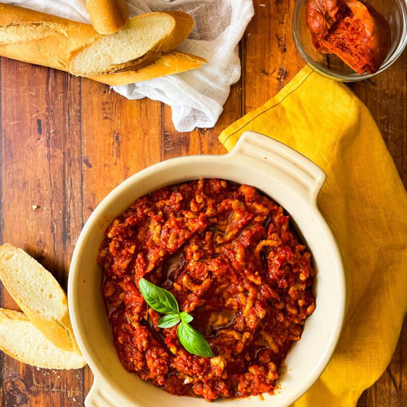 from top - nduja ragu in a pot with basil leaves on top, towel and bread around, nduja sausage in a pot, over a wooden background