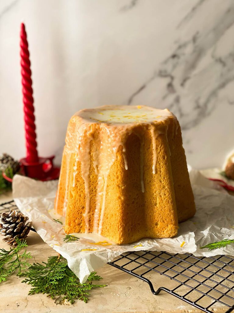 limoncello pandoro on a cooling rack with greenery, pinecones and a red candle