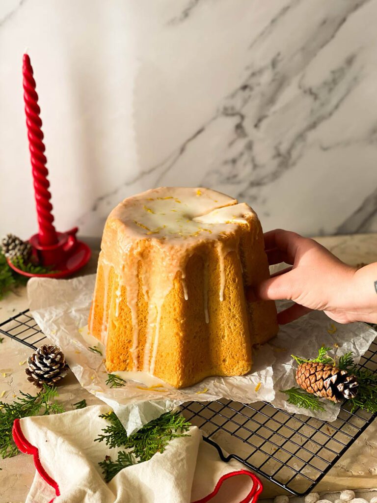 limoncello pandoro on a cooling rack with greenery, pinecones and a red candle