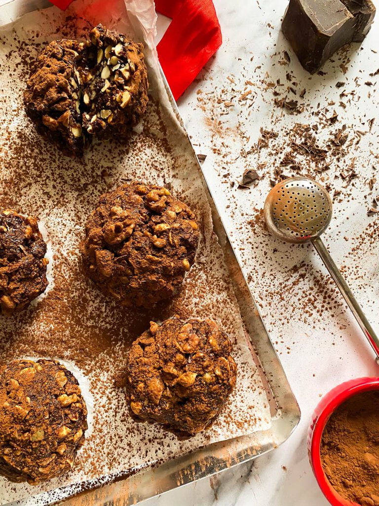panpepato on a baking tray over parchment paper, drizzled in cocoa powder, with a red ribbon and a chocolate chunk over a marble countertop