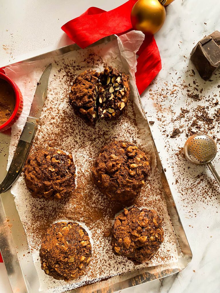 panpepato on a baking tray over parchment paper, drizzled in cocoa powder, with a red ribbon and a chocolate chunk over a marble countertop
