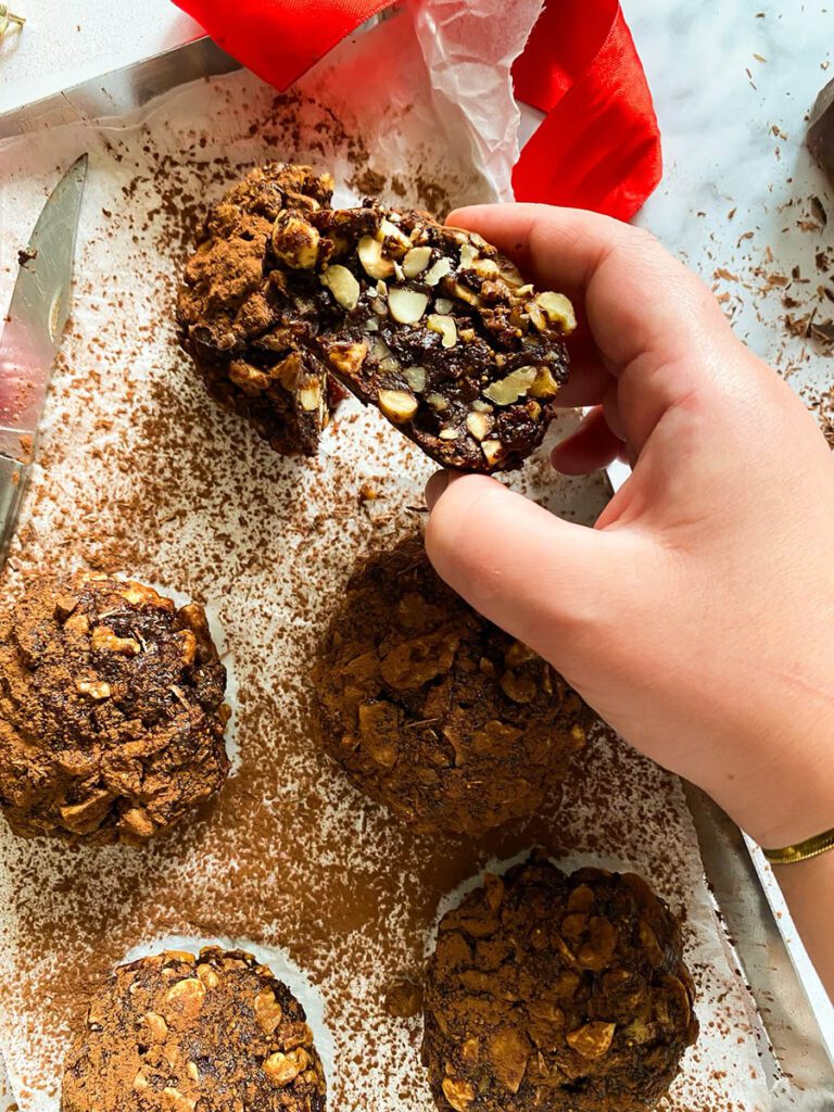 panpepato on a baking tray over parchment paper, drizzled in cocoa powder, with a red ribbon and a chocolate chunk over a marble countertop