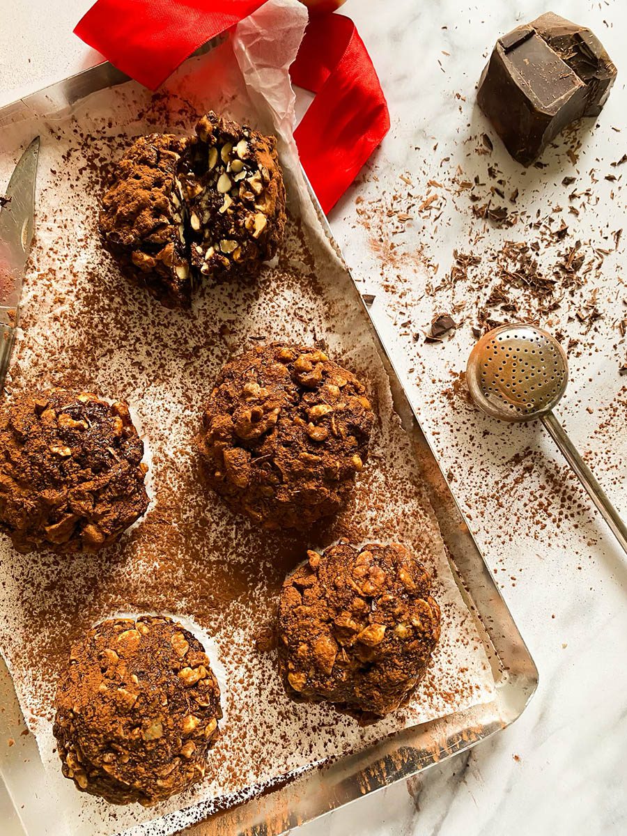 panpepato on a silver tray and parchment paper, cocoa powder, a red ribbon and chocolate around, on a marble background
