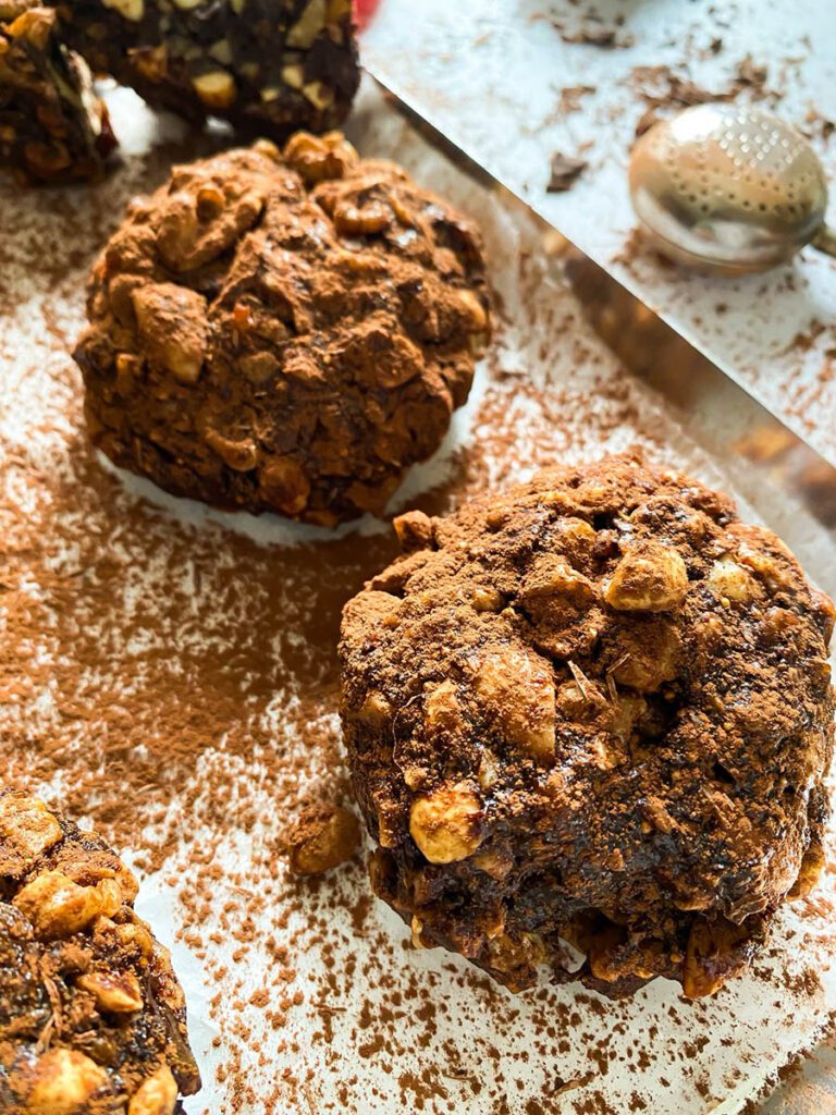panpepato on a baking tray over parchment paper, drizzled in cocoa powder, with a red ribbon and a chocolate chunk over a marble countertop