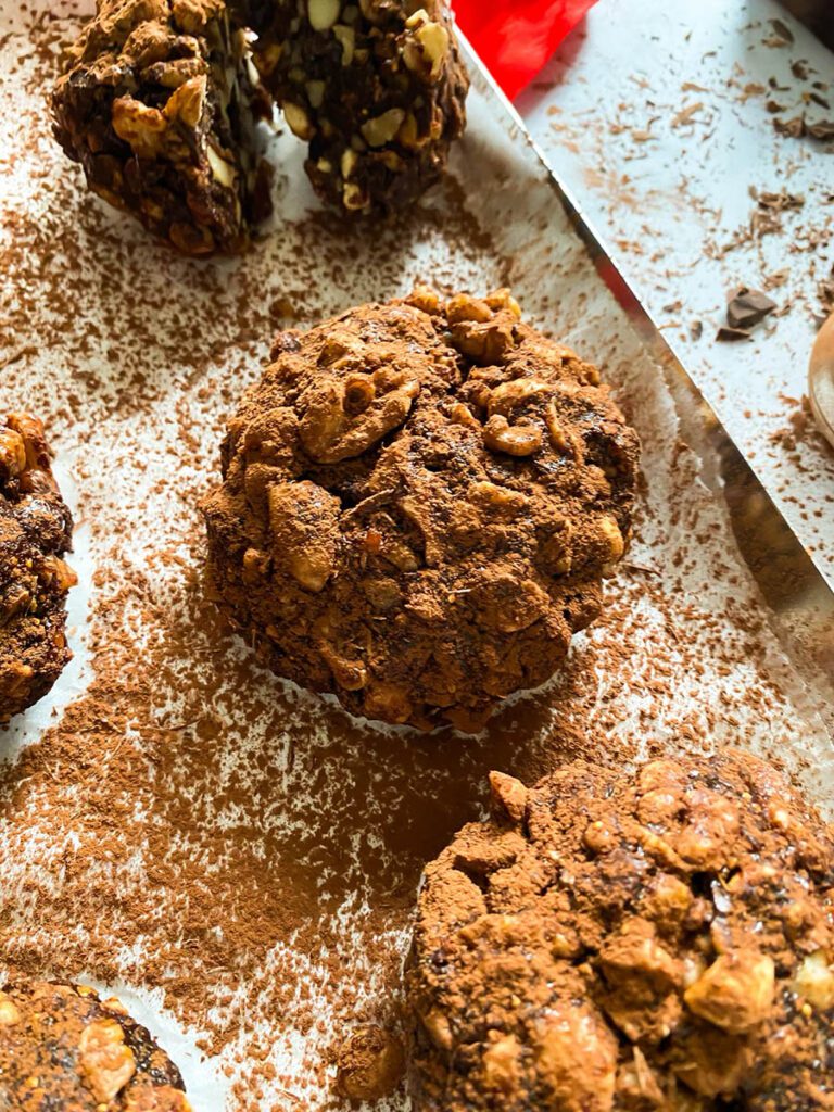panpepato on a baking tray over parchment paper, drizzled in cocoa powder, with a red ribbon and a chocolate chunk over a marble countertop