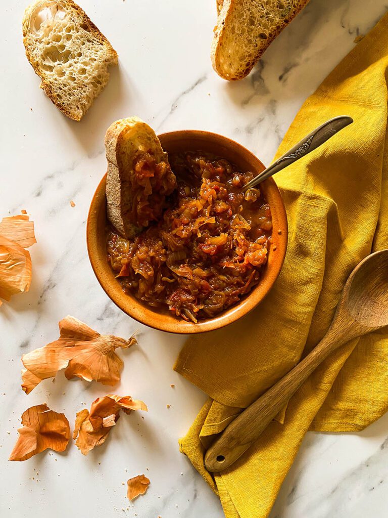 friggione in a terra cotta bowl with fresh bread scattered around on a yellow napkin