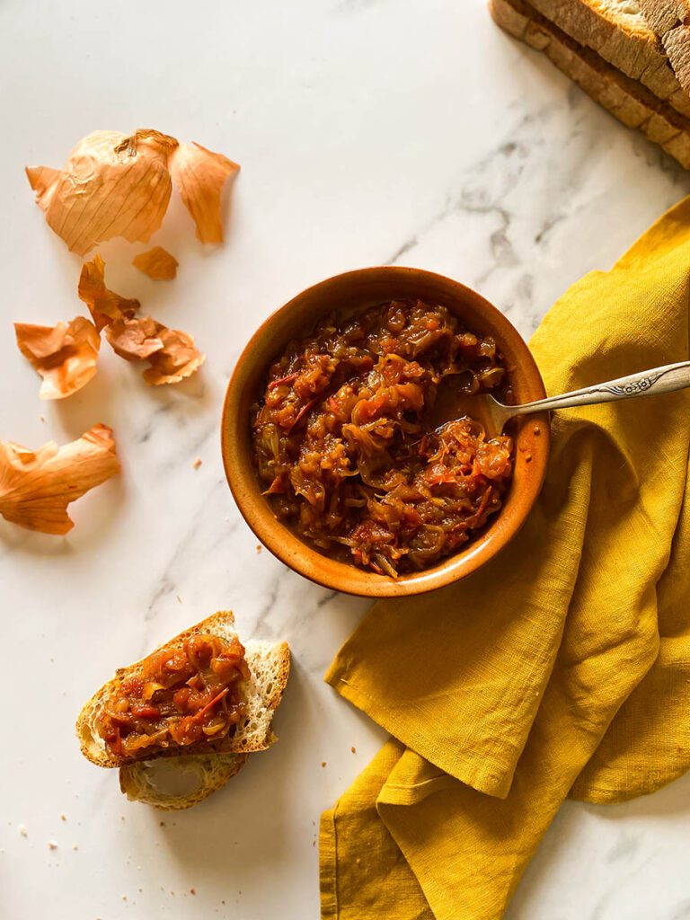 friggione in a terra cotta bowl with fresh bread scattered around on a yellow napkin
