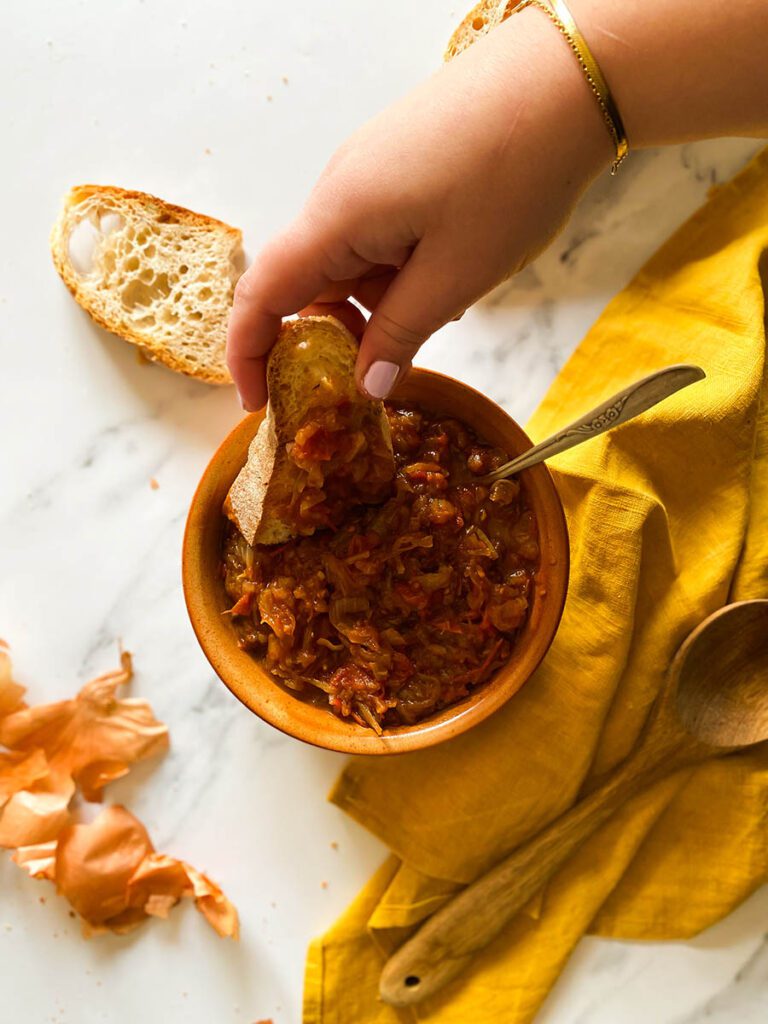 friggione in a terra cotta bowl with fresh bread scattered around on a yellow napkin