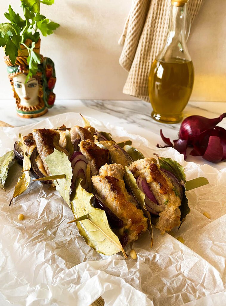 involtini alla siciliana over some bakoing paper with olive oil and red onion on the background