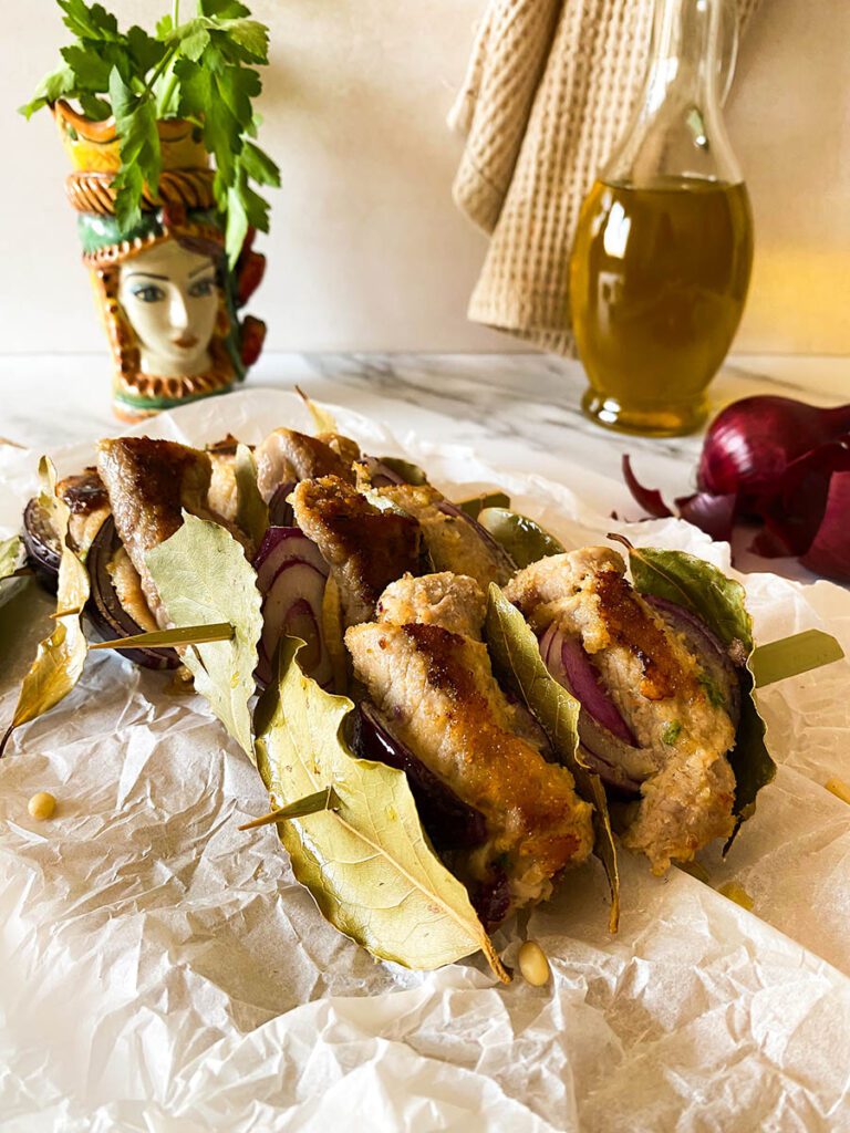 involtini alla siciliana over some bakoing paper with olive oil and red onion on the background