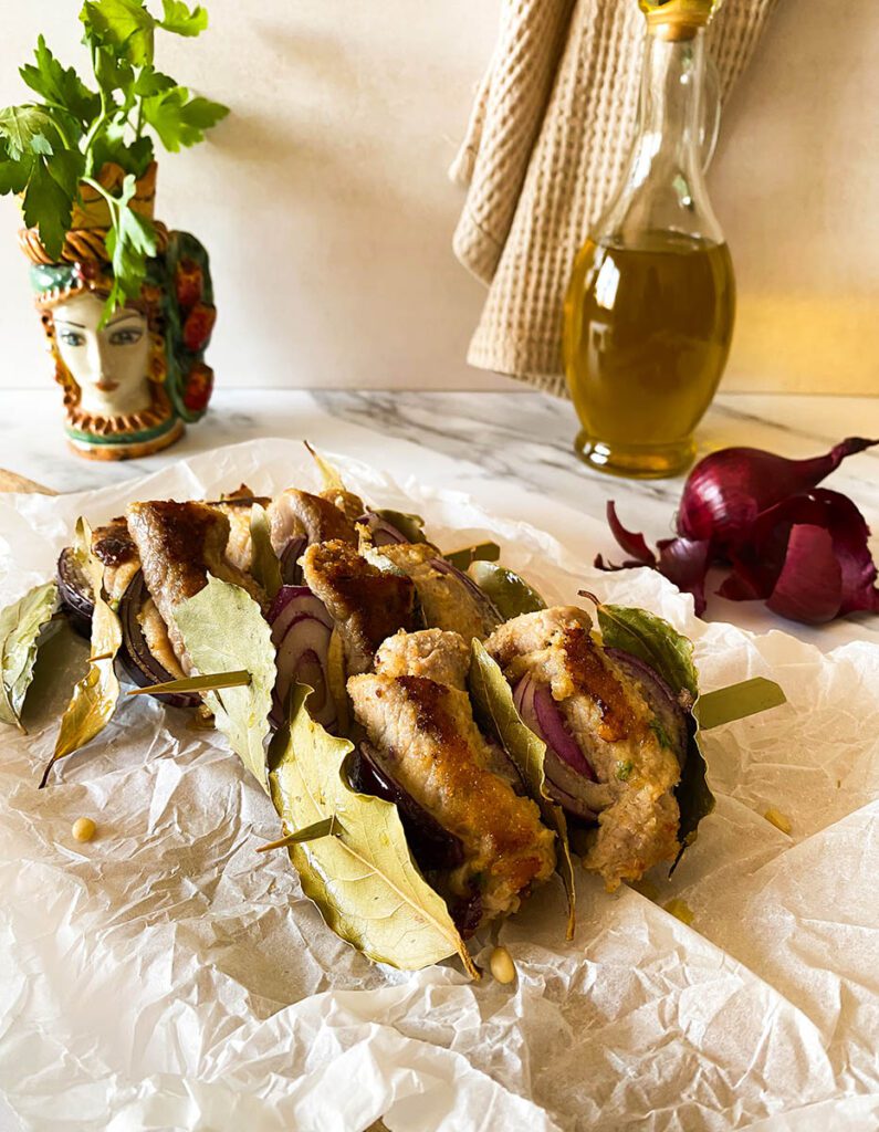involtini alla siciliana over some bakoing paper with olive oil and red onion on the background