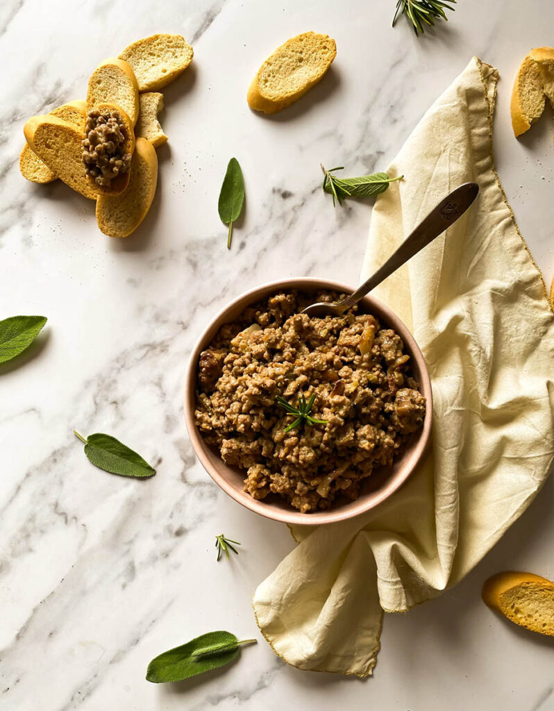 white ragu in a bowl, spoon in the bowl, towel on the side, on a marble background, crostini and sage leaves around