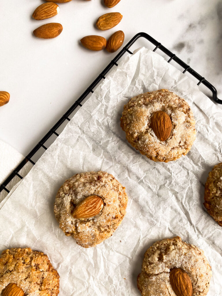 detail of amaretti sardi on parchment paper, laying on a grid, a white towel around, more almonds and sugar in pots