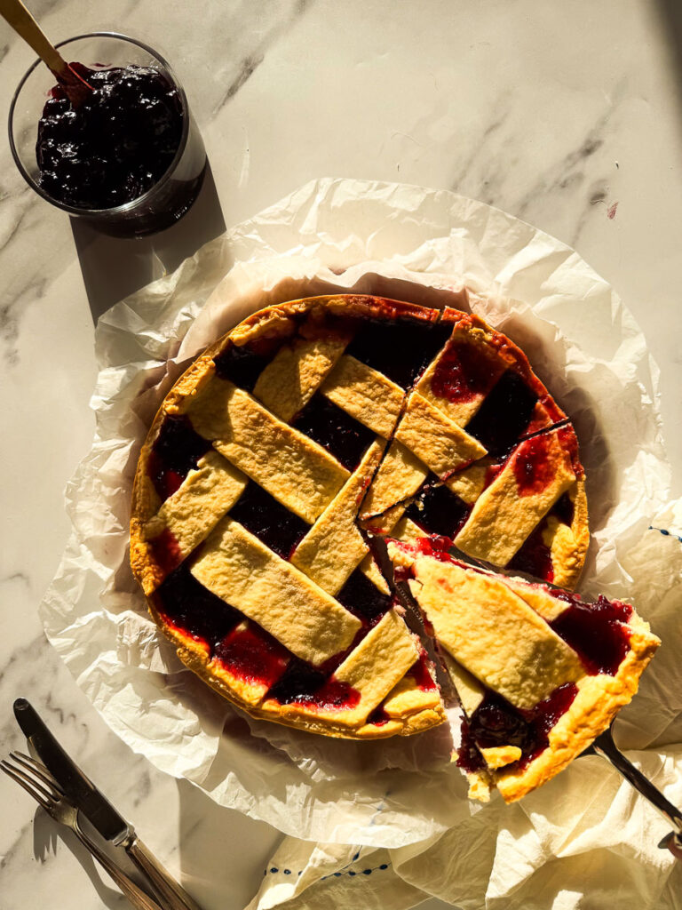 crostata on a marble background, jam on the side and cutlery, cut slices