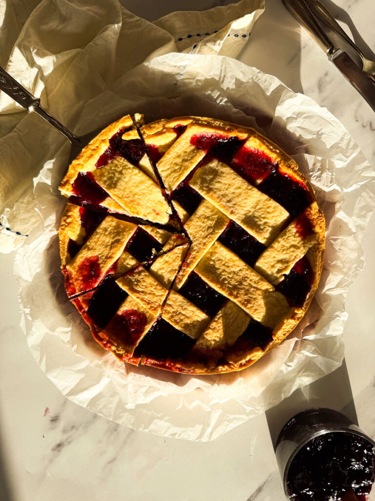 crostata on a marble background, jam on the side and cutlery, slices cut