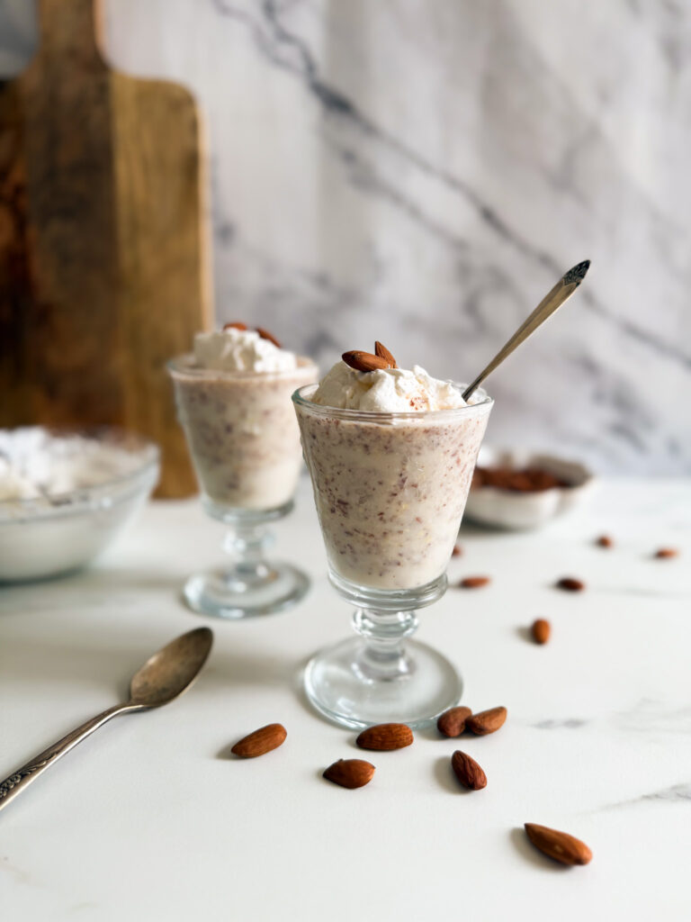 granita di mandorle in two tall glasses, spoon, almonds and cream in the background