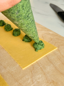 ricotta agnolotti recipe, hand filling the agnolotti with ricotta and spinach, on a wooden board, knife on the side, on marble background