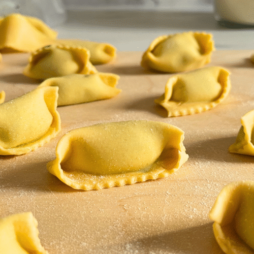 ricotta agnolotti, on a wooden board, on marble background, flour and filling in the back