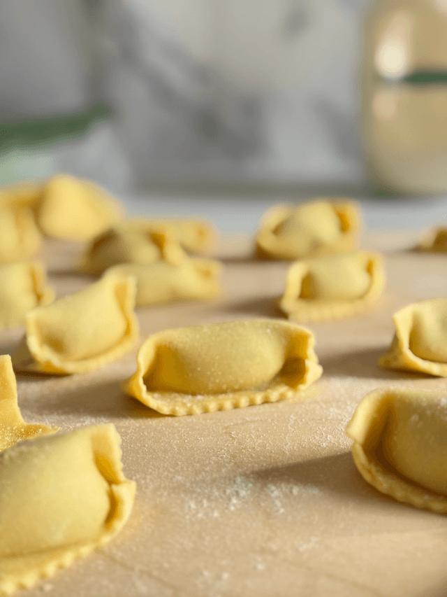 ricotta agnolotti, on a wooden board, on marble background, flour and filling in the back