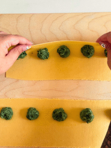 ricotta agnolotti recipe, hand folding the agnolotti with filling, wooden board under, on marble background