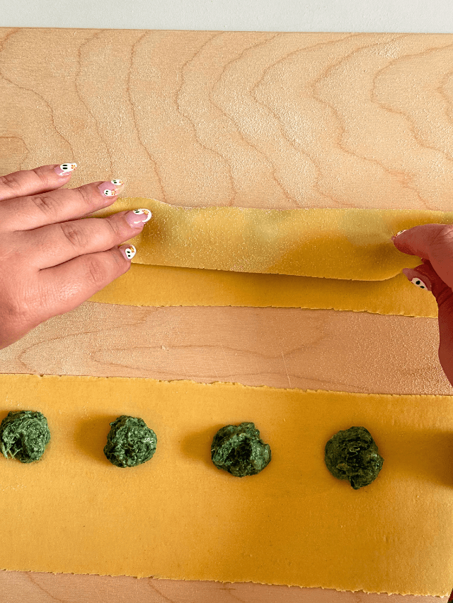 ricotta agnolotti recipe, hands folding the pasta sheet to make agnolotti, on wooden board, on marble background