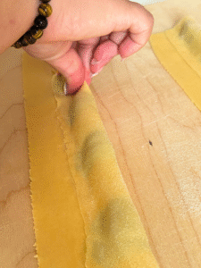 hand pinching the ricotta agnolotti, on a wooden board, on marble background