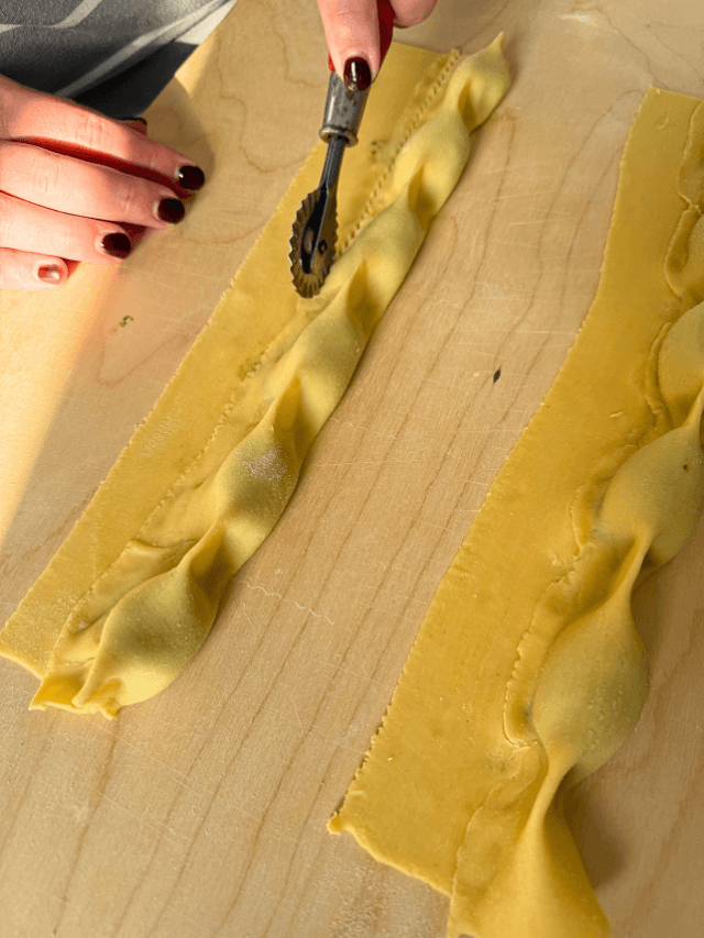 hand using a pasta cutter to cut the ricotta agnolotti, on wooden board