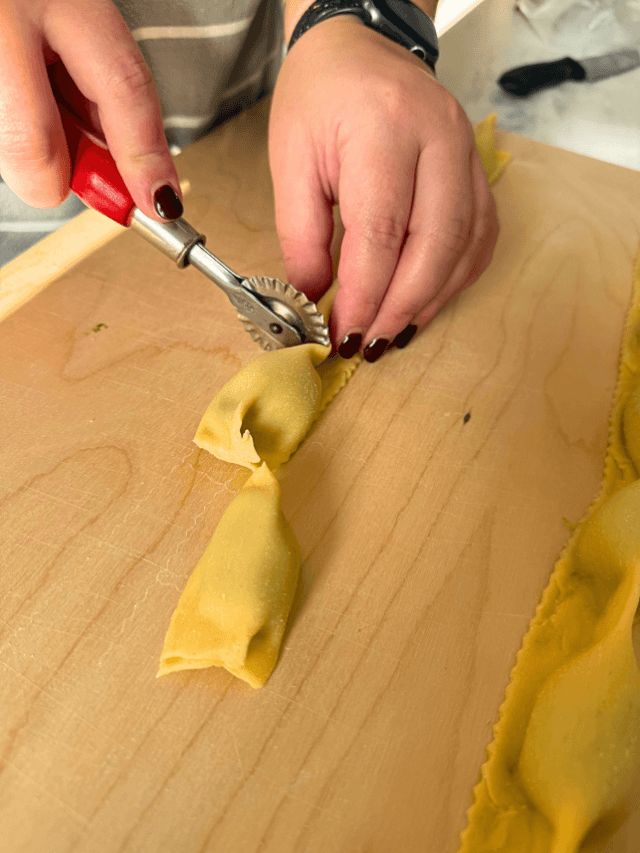 hand cutting the ricotta agnolotti with a pasta cutter, on a wooden board, on marble background, knife in the back