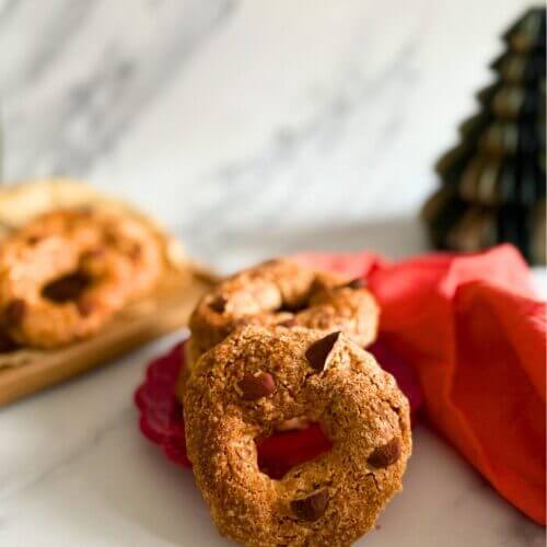 stack of roccocò cookies on a red towel, in the background more cookies on a wooden board and a christmas tree ornament, on a marble background