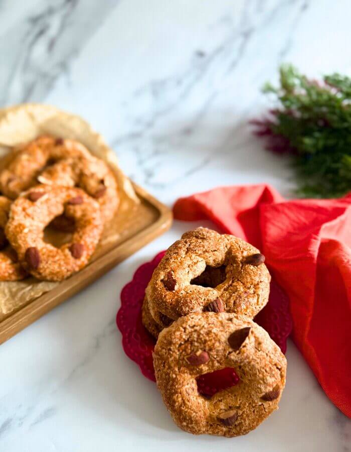 stack of roccocò cookies on a red plate and towel, in the background more cookies on a wooden board and a christmas ornament, on a marble background