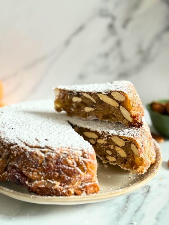 close up of panforte with a slice on top, on a plate, almonds on the side