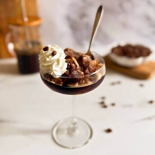 coupe of coffee granita granita al caffè with whipped cream, spoon in the granita, coffee beans in a pot and coffee pot in the background