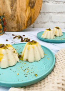Biancomangiare - a white pudding with pistachios and honey on top, 4 portions served in two light blue plates, on the background wooden board and a sicilian testa di moro in ceramic