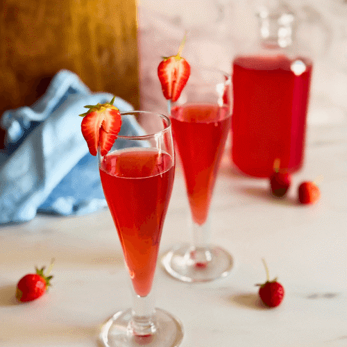 strawberry liqueur in two flute glasses, strawberries to decor, a bottle with liqueur, wooden board and a towel on the background