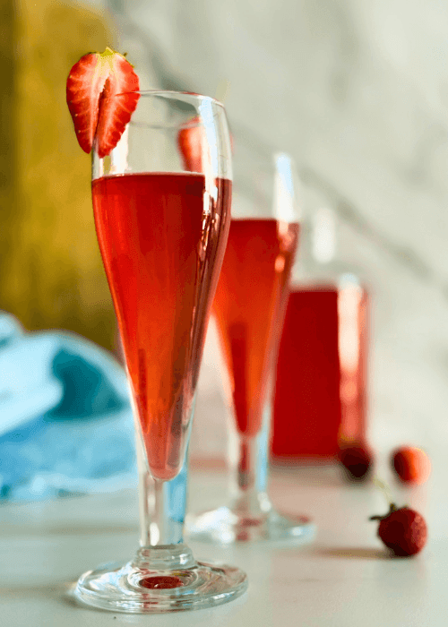 clos eup strawberry liqueur in two flute glasses, strawberries to decor, a bottle with liqueur, wooden board and a towel on the background