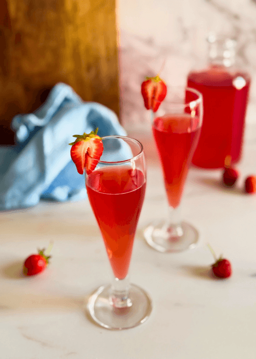 strawberry liqueur in two flute glasses, strawberries to decor, a bottle with liqueur, wooden board and a towel on the background